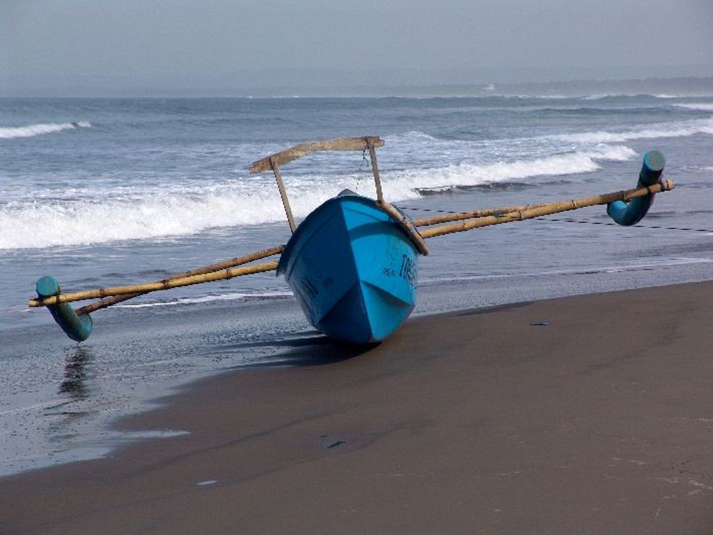 Blauwe vissersboot op het strand bij de branding tijdens familiereis Sumatra, Java en Bali.