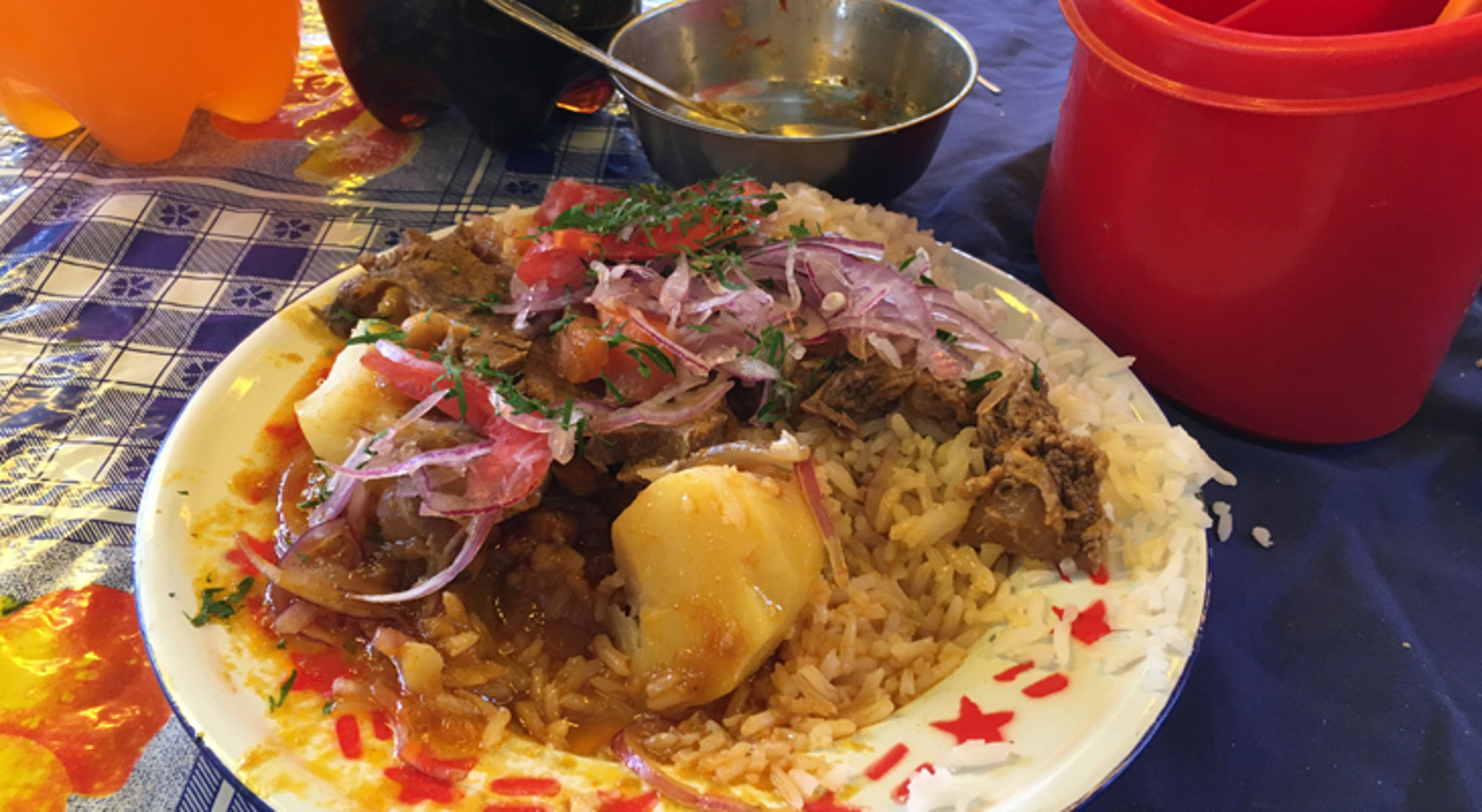 boliviaanse maaltijd Bord met rijst, stoofvlees en aardappel, gegarneerd met rode ui en tomaat op een tafelkleed.