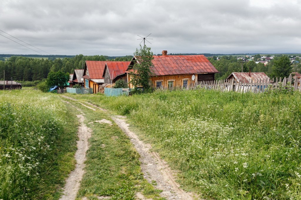 Houten huizen met rode daken langs een zandpad in het Russische platteland tijdens de Trans-Siberië Expres rondreis.
