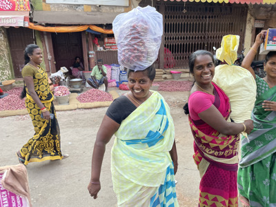 Vrouwen in kleurrijke sari’s op een markt in Zuid-India met zakken en manden vol uien op de achtergrond.