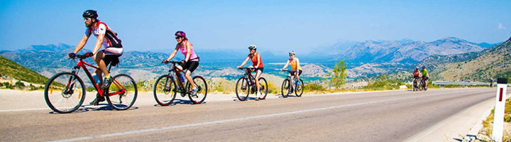 Fietsers op een bergweg met uitzicht op een vallei en bergketens tijdens een fietstocht in Europa.