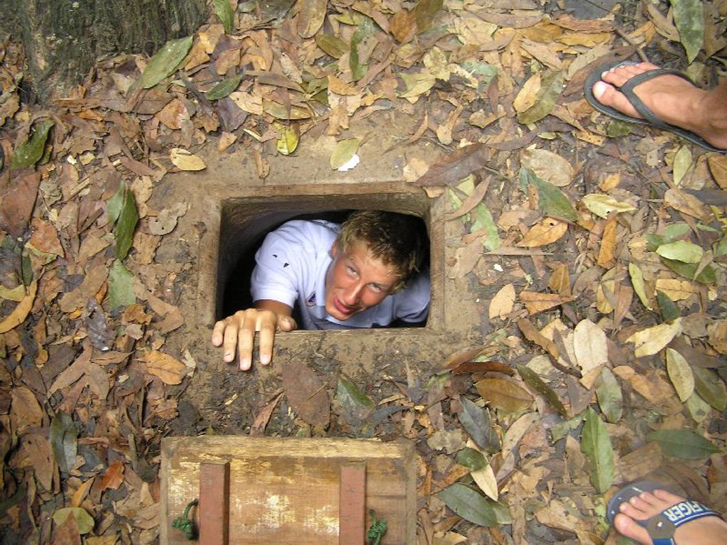 Reiziger kruipt uit een smalle ondergrondse tunnelopening in Vietnam tijdens groepsrondreis Vietnam kort.