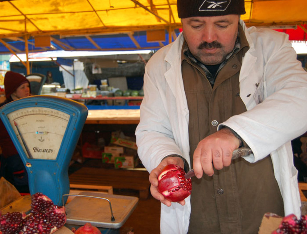 Marktkoopman snijdt een granaatappel op een Russische markt tijdens groepsrondreis Rusland.