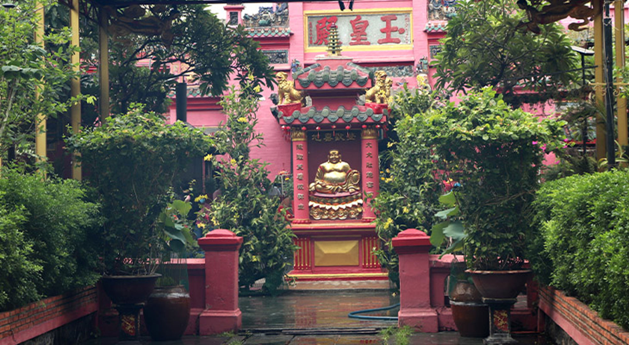 Ho Chi Minhstad Boeddhabeeld bij een kleurrijke Chinese tempel, omringd door groen.