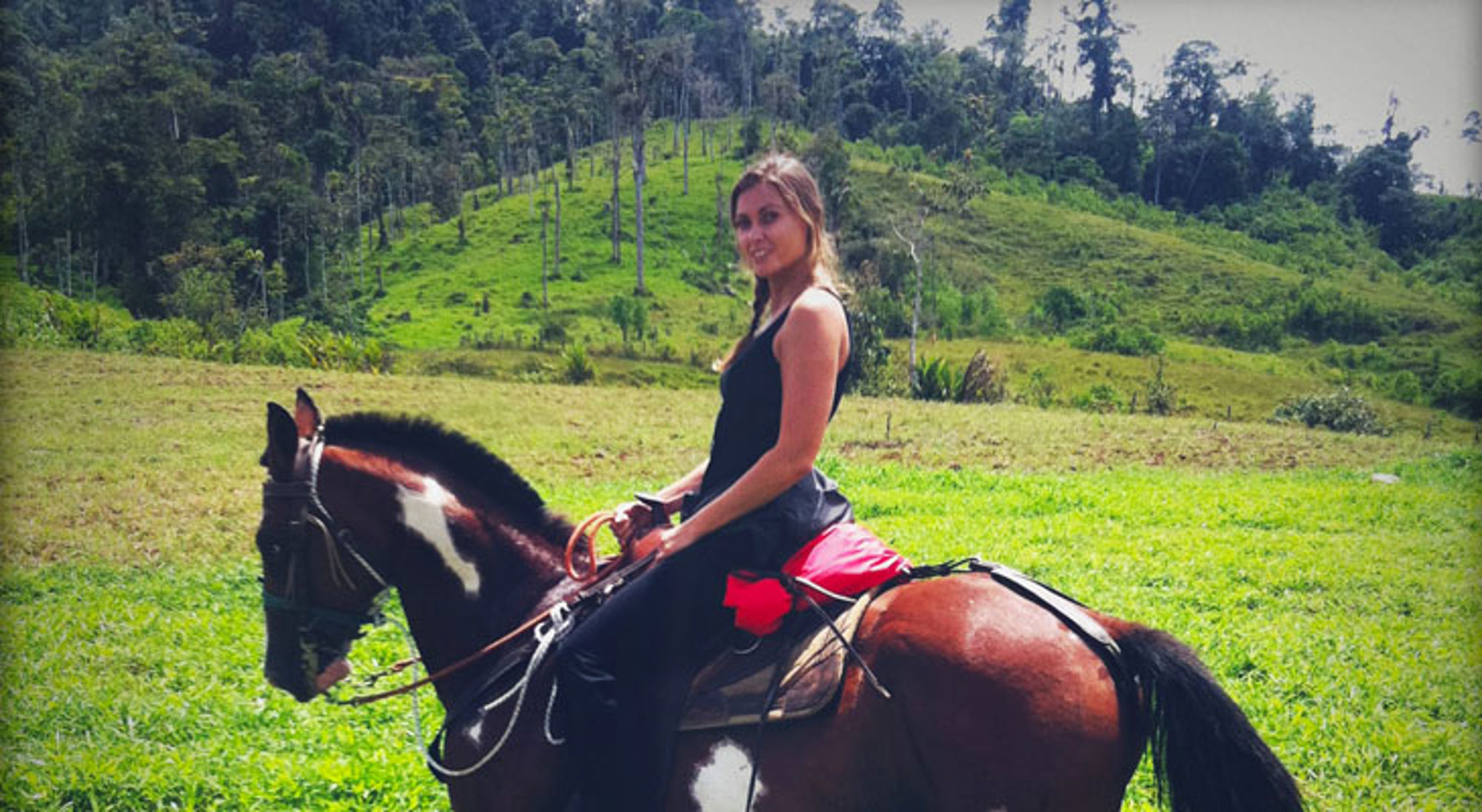 Vrouw te paard in een groen heuvelachtig landschap tijdens een buitenrit.