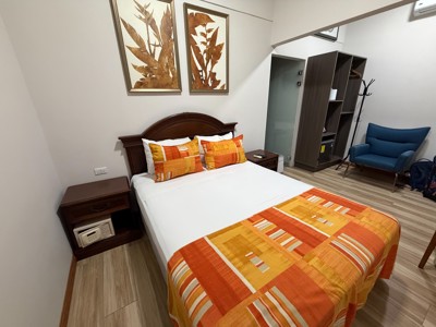 Tweepersoonskamer bij Eco Arenal in Costa Rica met tweepersoonsbed, kast en blauwe stoel.