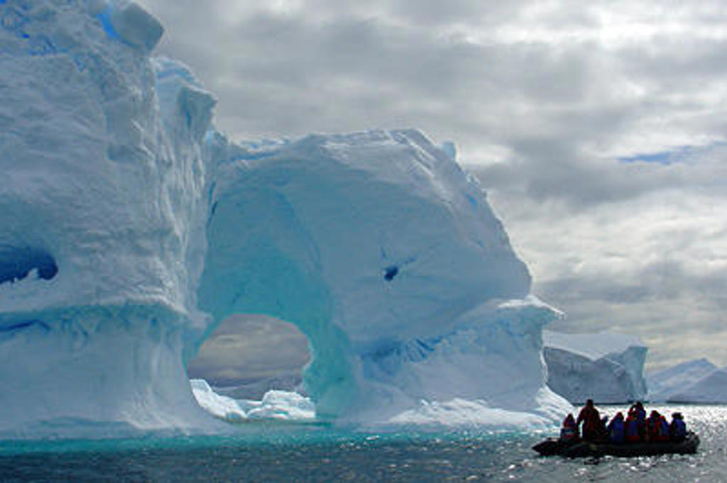 Zodiacboot met expeditiegroep langs een enorme ijsberg in Antarctica, tijdens Crossing the Circle voorbij de zuidpoolcirkel.