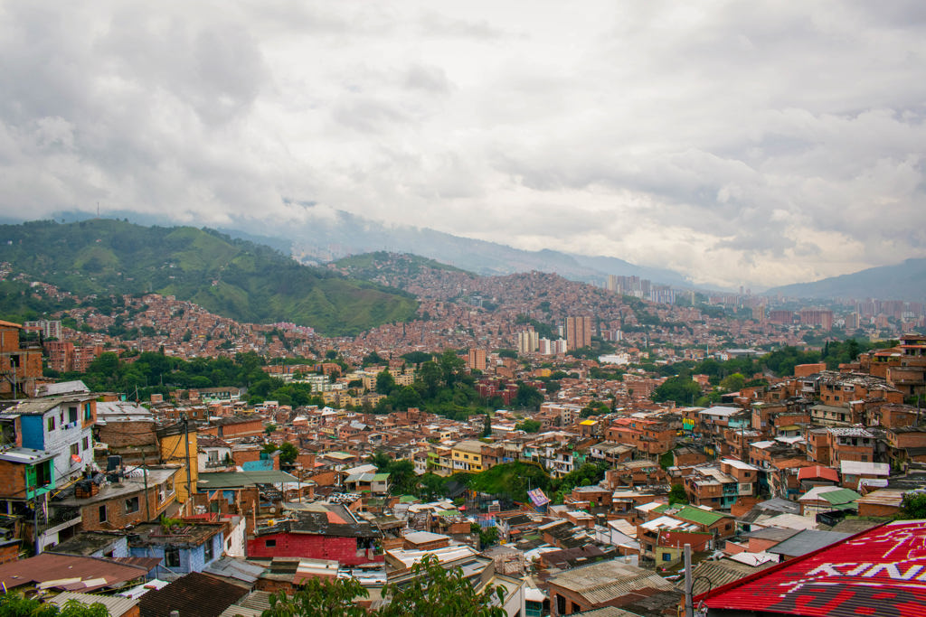 Uitzicht over Medellín met kleurrijke wijken op de heuvels en groene bergen onder een bewolkte lucht.