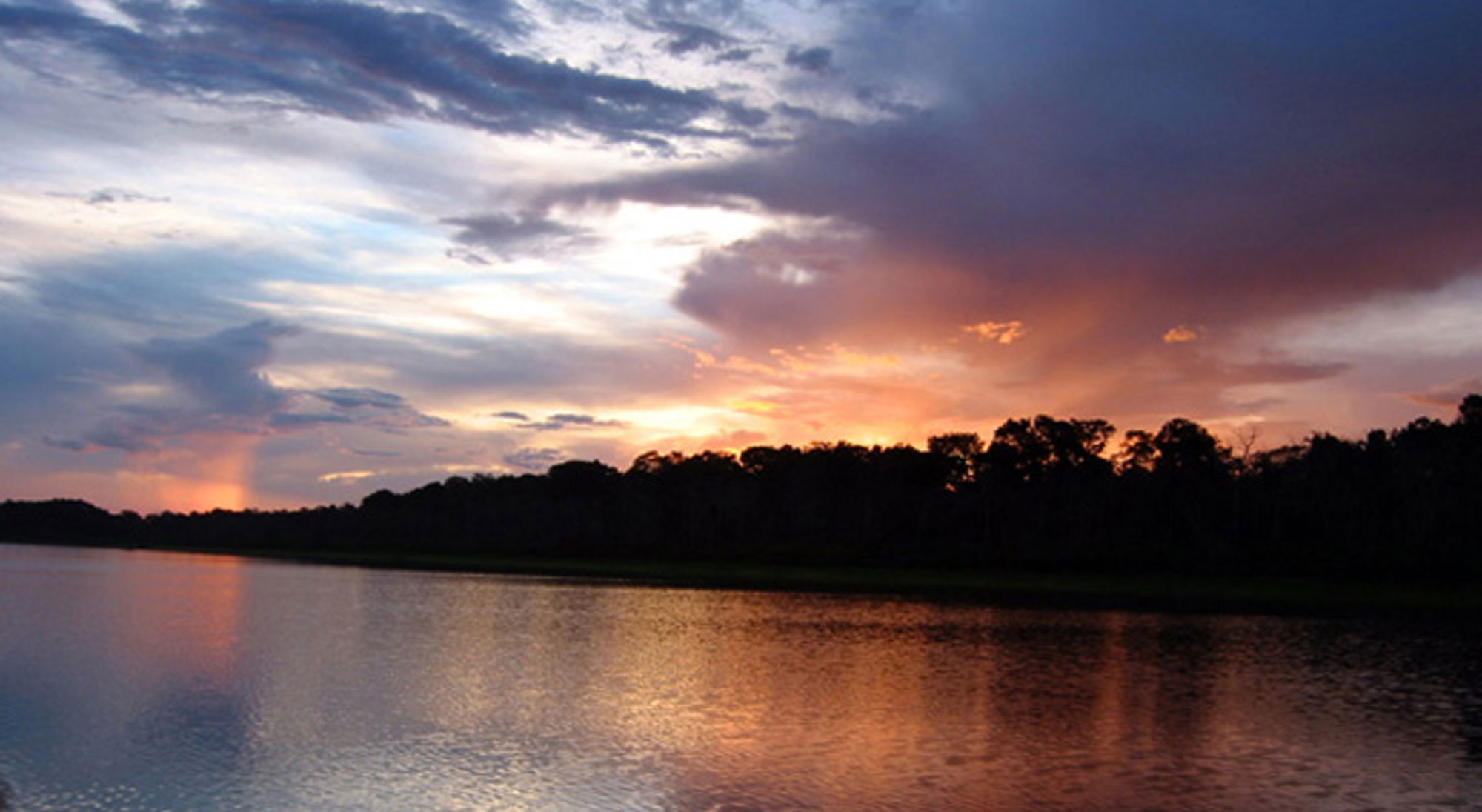 Amazone Zonsondergang boven een rivier met silhouetten van bomen en kleurrijke wolkenlucht in Colombia.