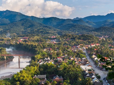 Uitzicht over Luang Prabang aan de Mekong, met brug, tempeldaken en groene bergen op de achtergrond.