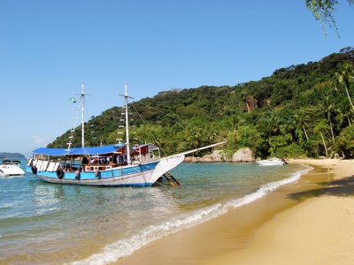 Schoener voor anker bij een tropisch strand in Brazilië, met groene heuvels op de achtergrond.