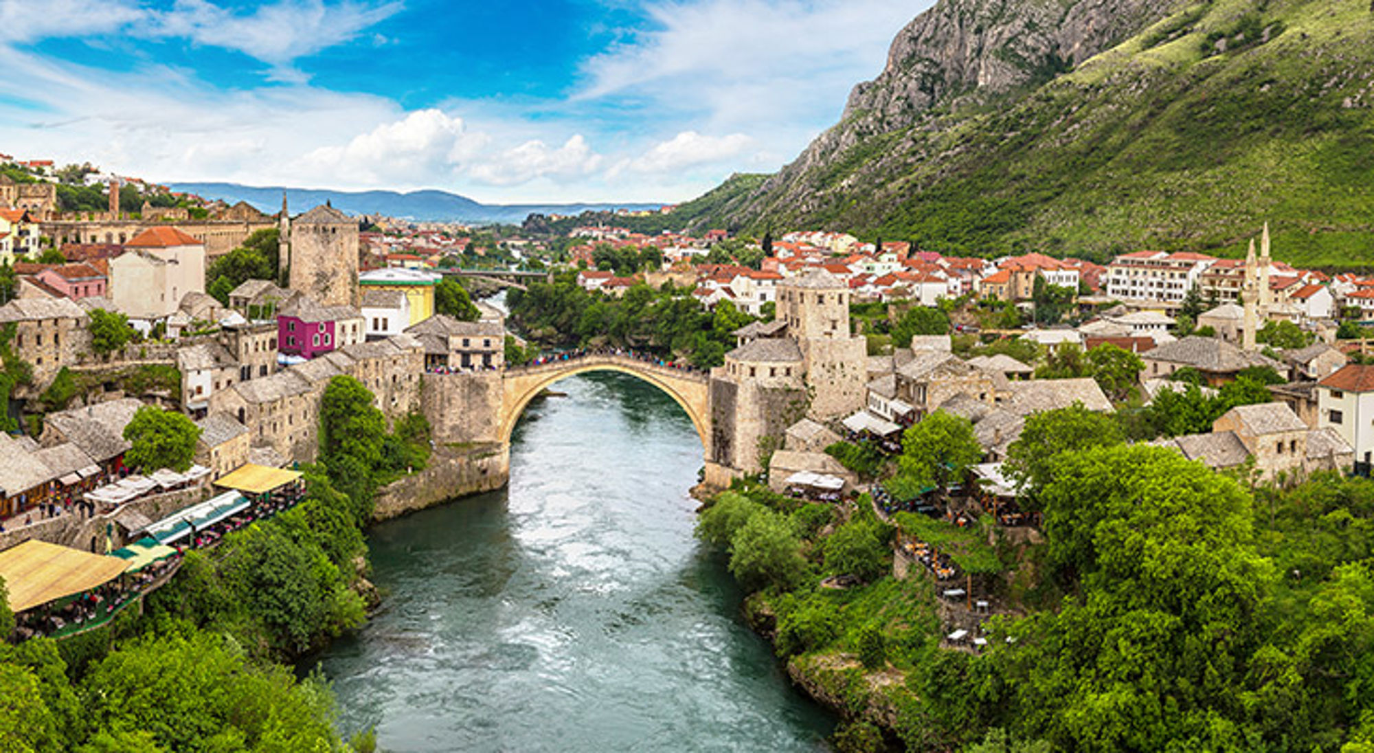 Uitzicht over Mostar in Bosnië Uitzicht op de Stari Most-brug over de Neretva in Mostar, met oude stad en groene bergen op de achtergrond.