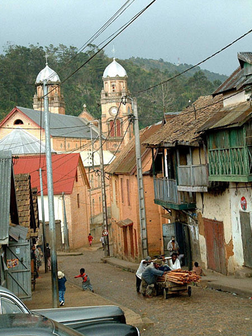 Straatbeeld in Madagascar met kleurrijke huizen en een kerk met koepels op de achtergrond.