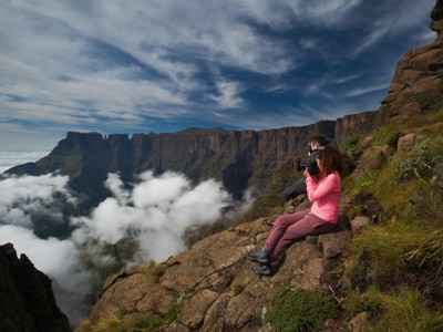 Wandelaars fotograferen het uitzicht over de Drakensbergen in Zuid-Afrika, met wolken in de vallei en steile rotswanden.