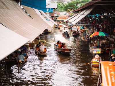Drijvende markt in Thailand met boten vol etenswaren onder kleurrijke parasols op een smalle gracht.