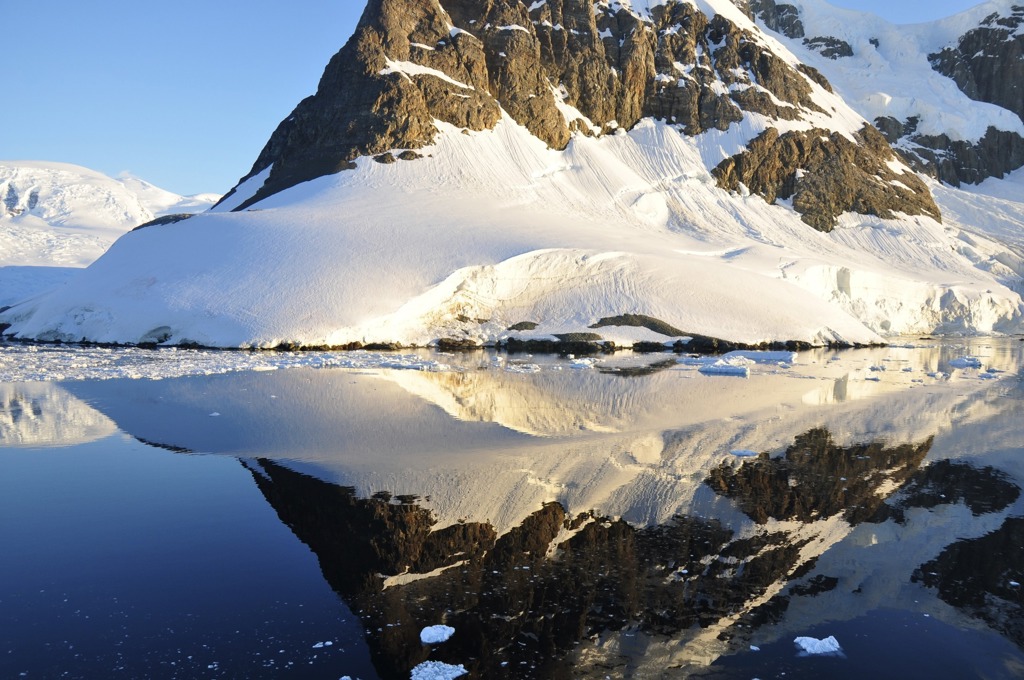 Sneeuwbedekte berg en gletsjer in Antarctica, weerspiegeld in het stille water met drijvend ijs.