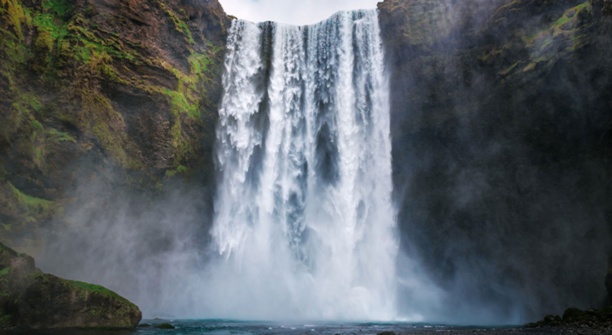 Skogafoss waterval in IJsland Waterval die met veel nevel naar beneden stort tussen groene rotswanden.