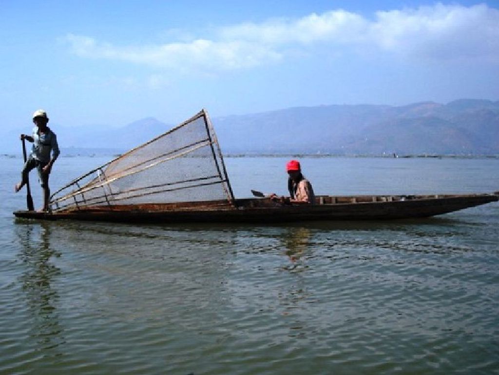 Vissers in een houten boot op Inle Lake in Myanmar, met visnet en bergen op de achtergrond.