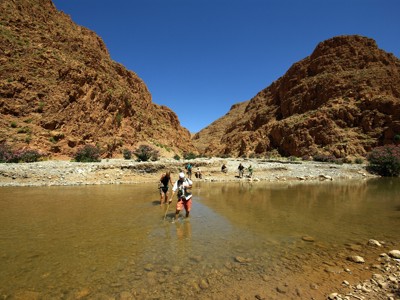 Gezin wandelt door een ondiepe rivier in een rotsachtige kloof tijdens de Route Marokko Familiereis.