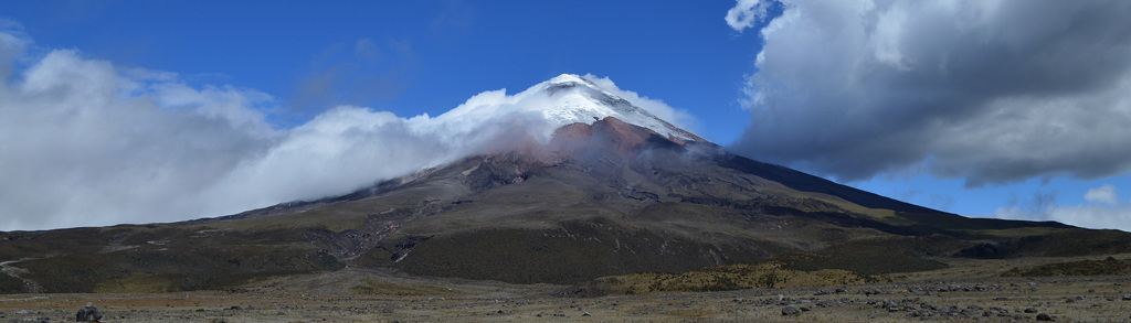 Sneeuwbedekte vulkaan Cotopaxi in Ecuador, omringd door wolken en hooglandlandschap.