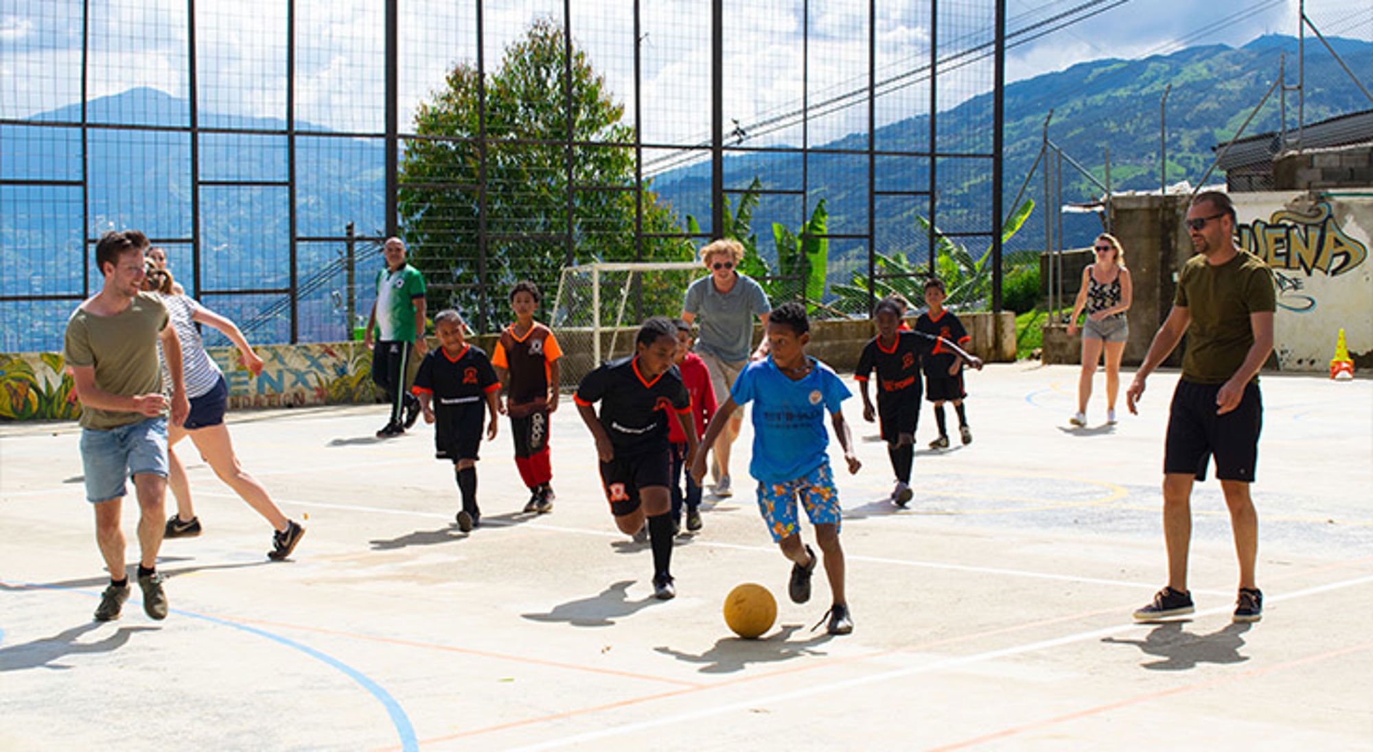Sawadee reizigers voetballen bij Stichting Children of Medellín Kinderen spelen voetbal op een sportveld met bergen op de achtergrond.