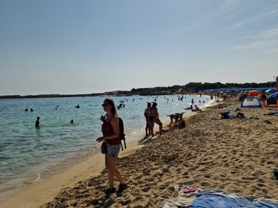 Druk zandstrand op Cyprus met zwemmers in helderblauw water en strandgangers onder parasols.