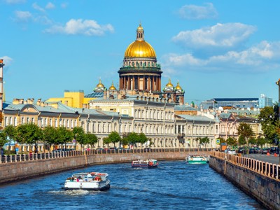 Izaäkkathedraal met gouden koepel aan het kanaal in Sint-Petersburg, met rondvaartboten op het water.