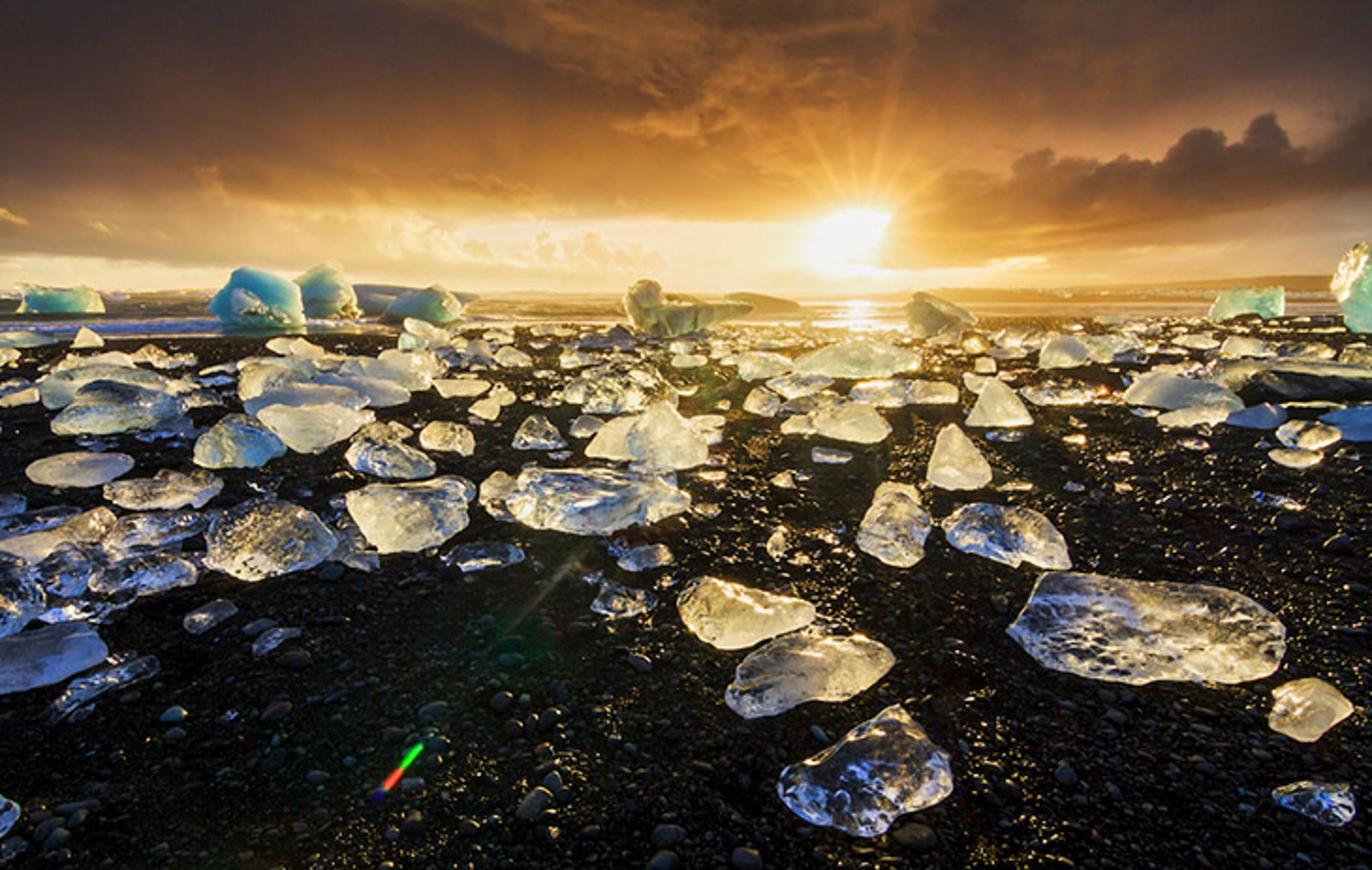 IJsland in de winter Zonsondergang boven een zwart strand met verspreide ijsbrokken langs de kust.