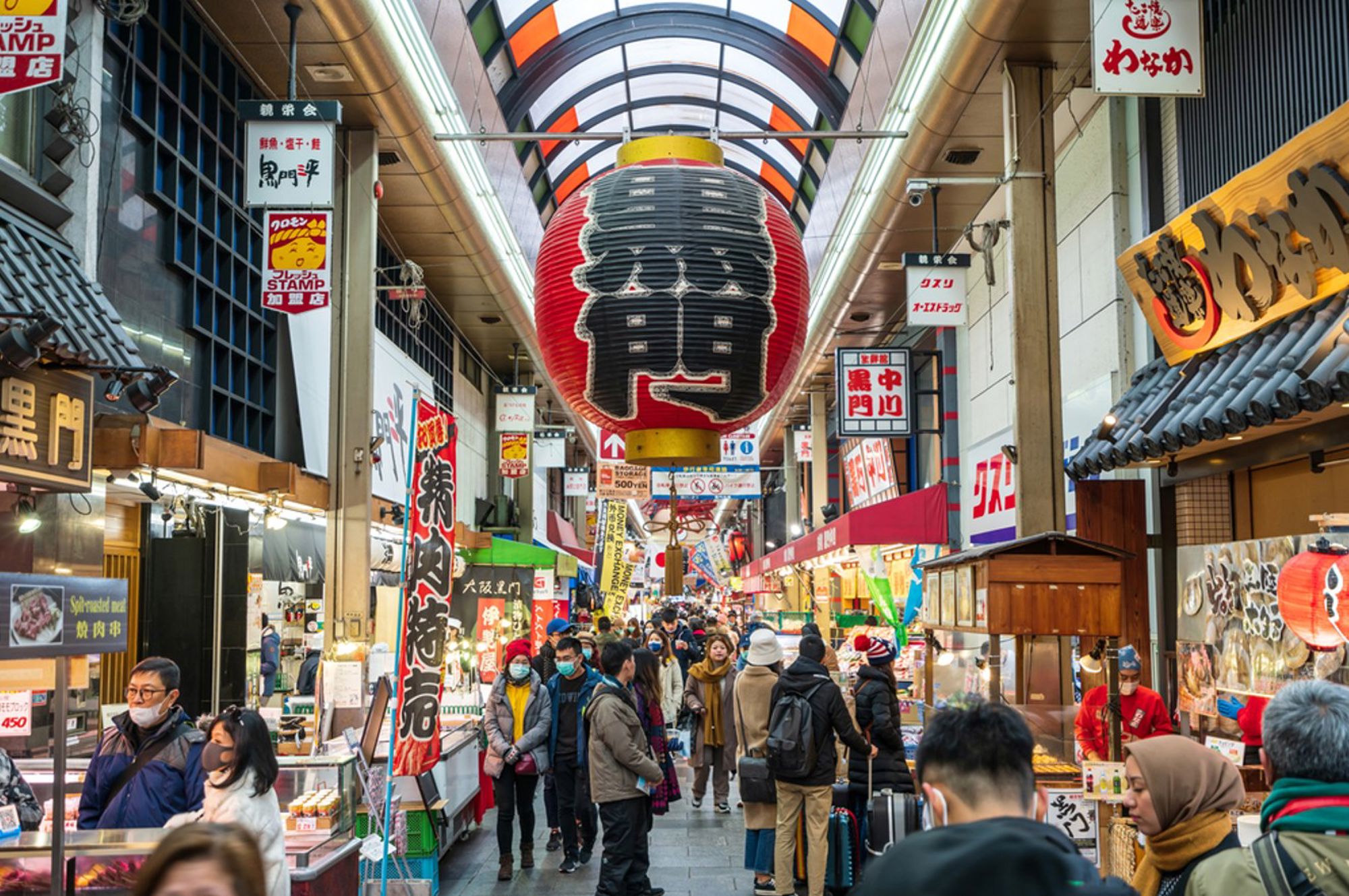 Drukke overdekte winkelstraat in Japan met grote rode lantaarn en marktkramen.