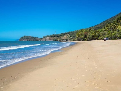 Breed zandstrand met palmbomen en zachte golven aan de kust van Australië tijdens de 21-daagse kampeer- & hotelreis.