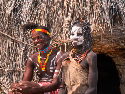 Twee bewoners in traditionele kleding met lichaamsbeschildering bij een rieten hut in Ethiopië.