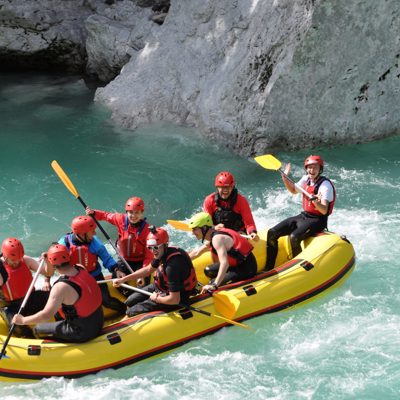 Groep rafters in een gele raftboot op de turquoise Soca rivier tijdens een excursie.