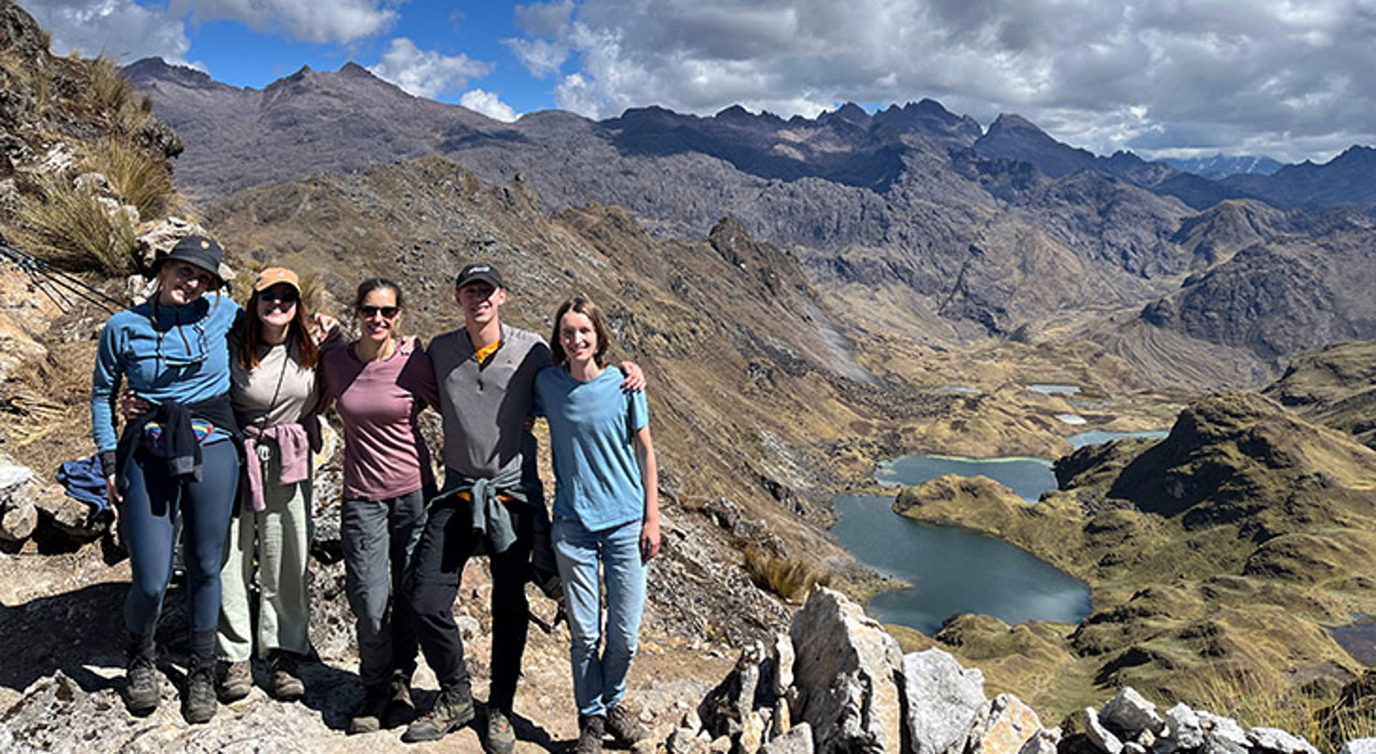 Hiken Peru Vijf wandelaars poseren op een bergkam met uitzicht op een vallei met meren en ruige bergtoppen.