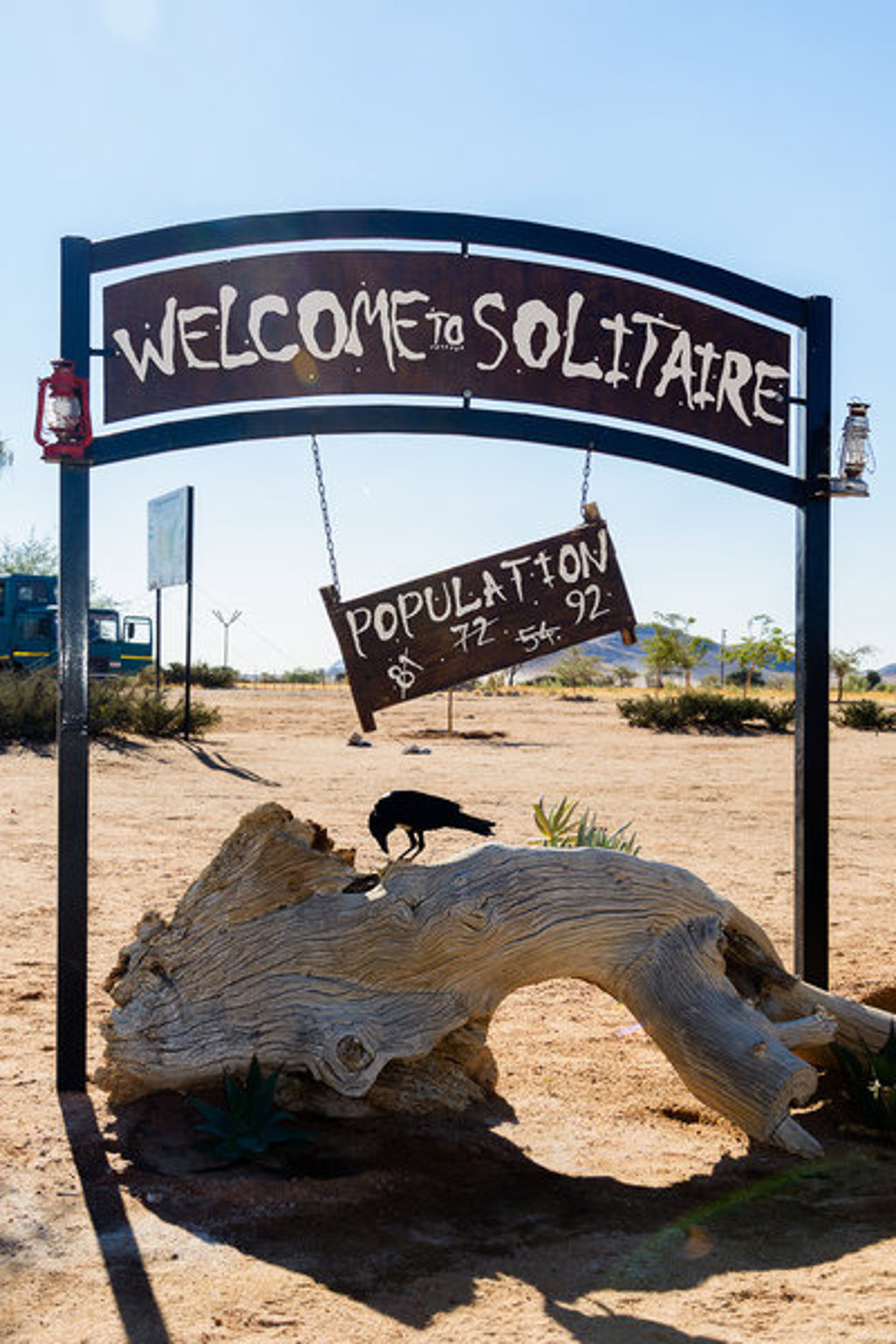 Welkomstbord van Solitaire in Namibië, met een vogel op een boomstam in de woestijn.