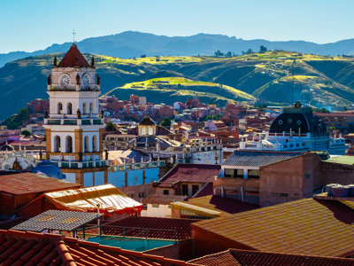 Uitzicht over Sucre in Bolivia met klokkentoren en daken, met groene heuvels op de achtergrond.