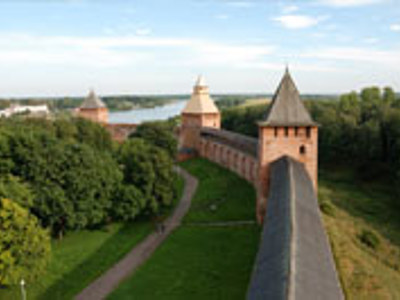 Middeleeuwse vestingmuur met torens in Veliki Novgorod, omringd door groen en met rivier op de achtergrond.