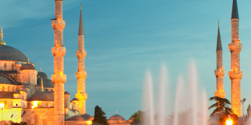 Blauwe Moskee in Istanbul bij zonsondergang, met verlichte minaretten en fontein op de voorgrond.