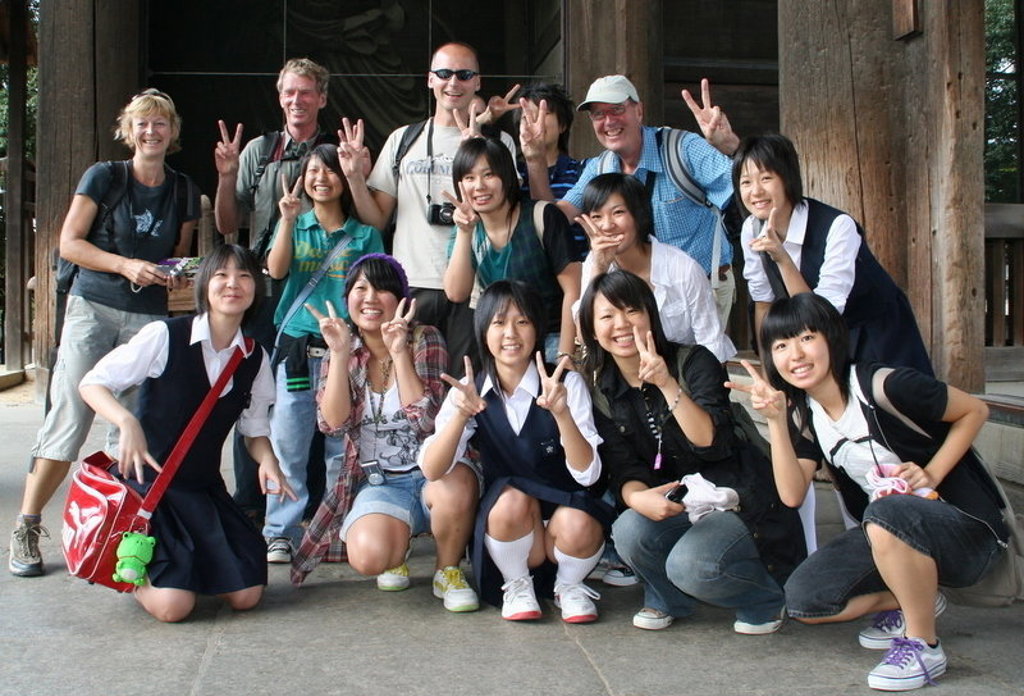 Groepsrondreis Japan: reizigers poseren met lokale jongeren bij een tempel en maken een vredesteken.