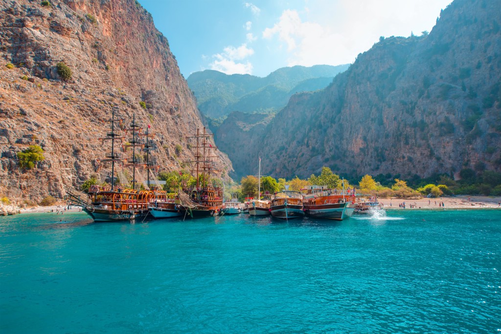 Piratenboten aan een strand in een baai met turquoise water en hoge rotswanden aan de Turkse kust.