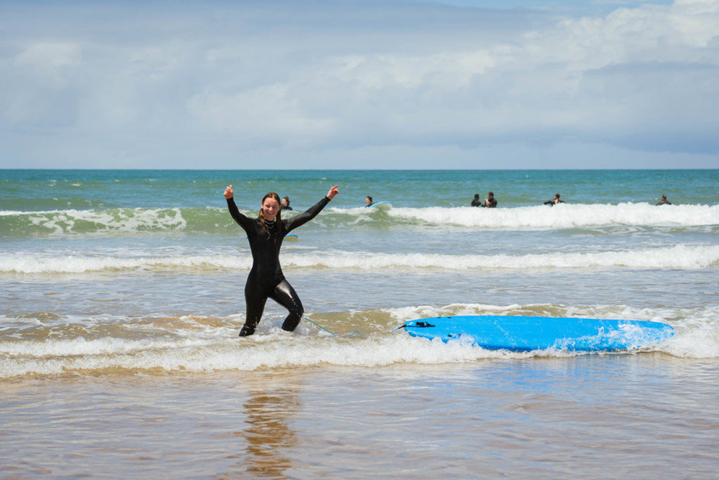 Surfer in wetsuit viert een geslaagde surfles op het strand in Marokko tijdens een 22-35ers reis.