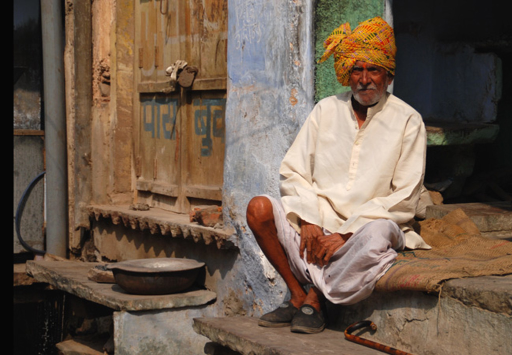 Man met kleurrijke tulband zit voor een huis in Gujarat, India.