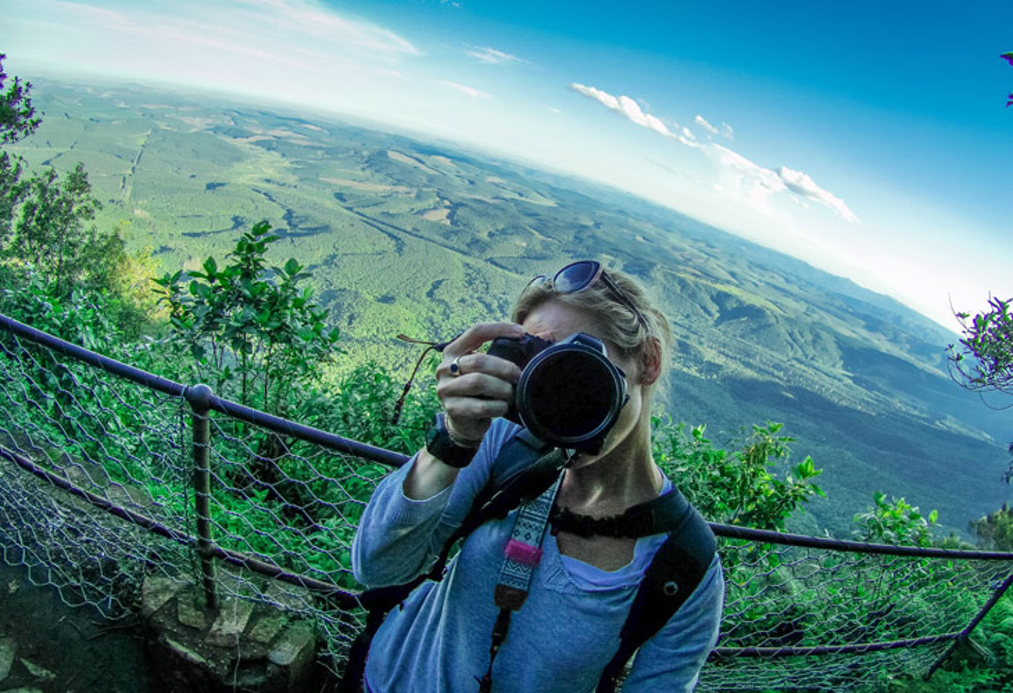 Vrouw maakt foto bij uitzichtpunt met panoramisch uitzicht over groene heuvels en valleien.