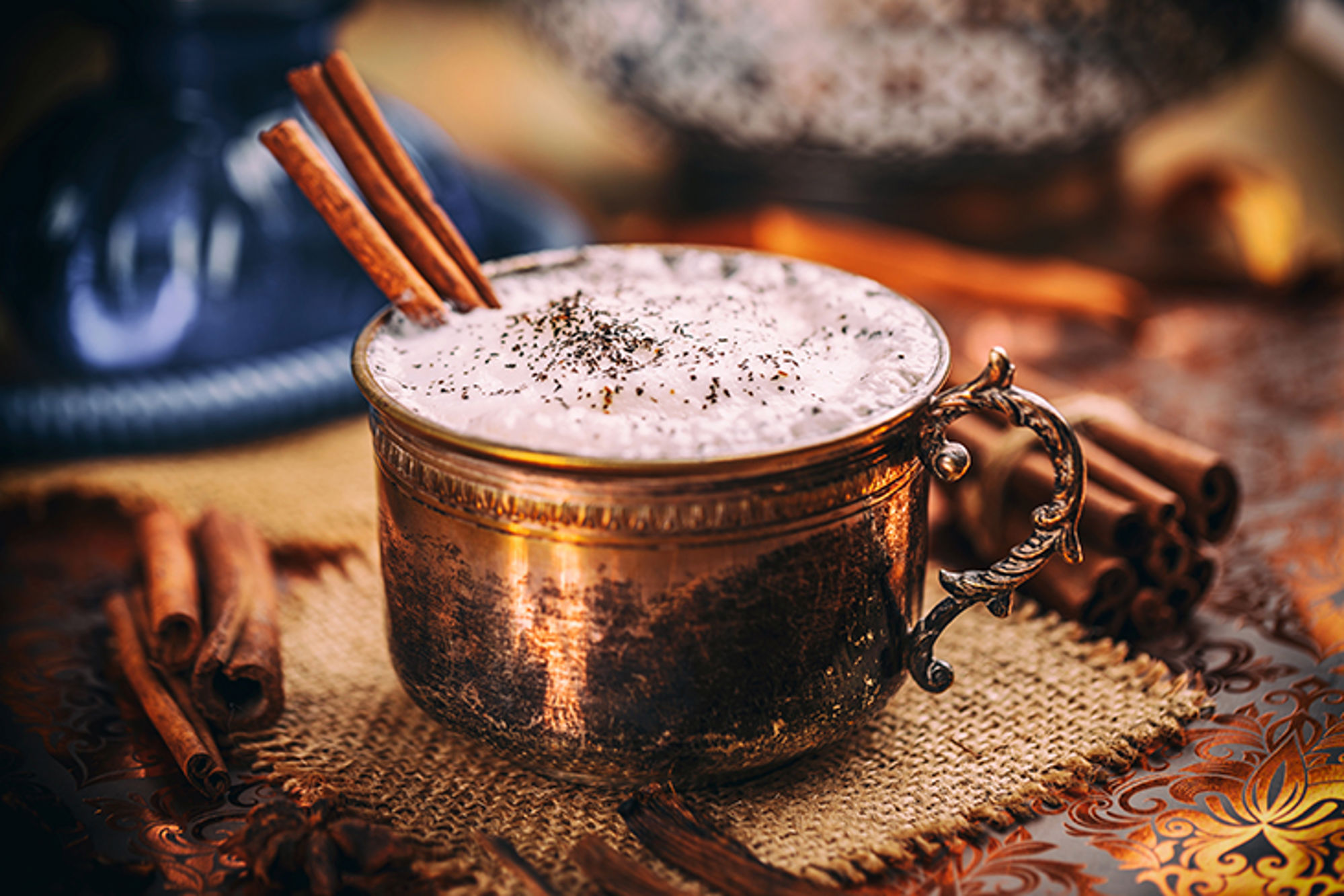 Koperen mok met romige chai latte, kaneelstokjes en specerijen op tafel.