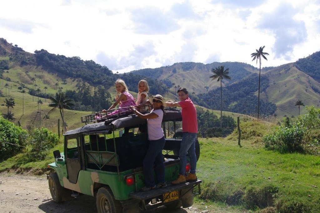 Gezin op een jeep met uitzicht op groene bergen en hoge palmbomen tijdens een familiereis Colombia.