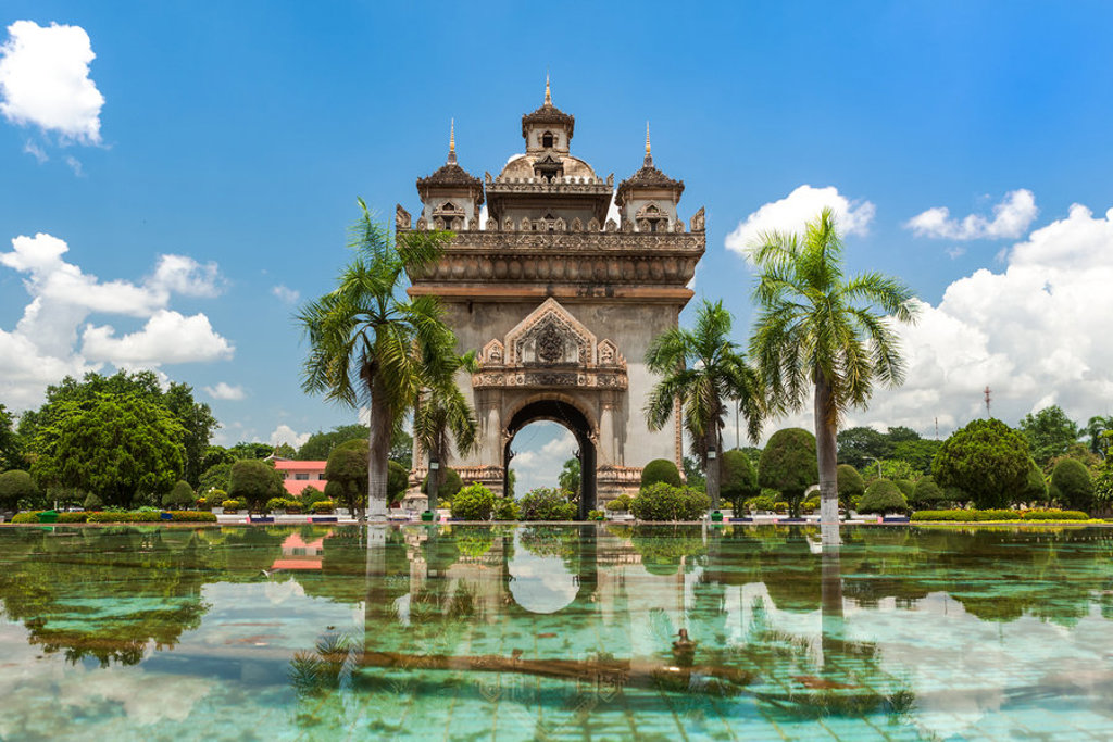 Patuxai-monument in Vientiane, Laos, met palmbomen en spiegeling in de fontein.