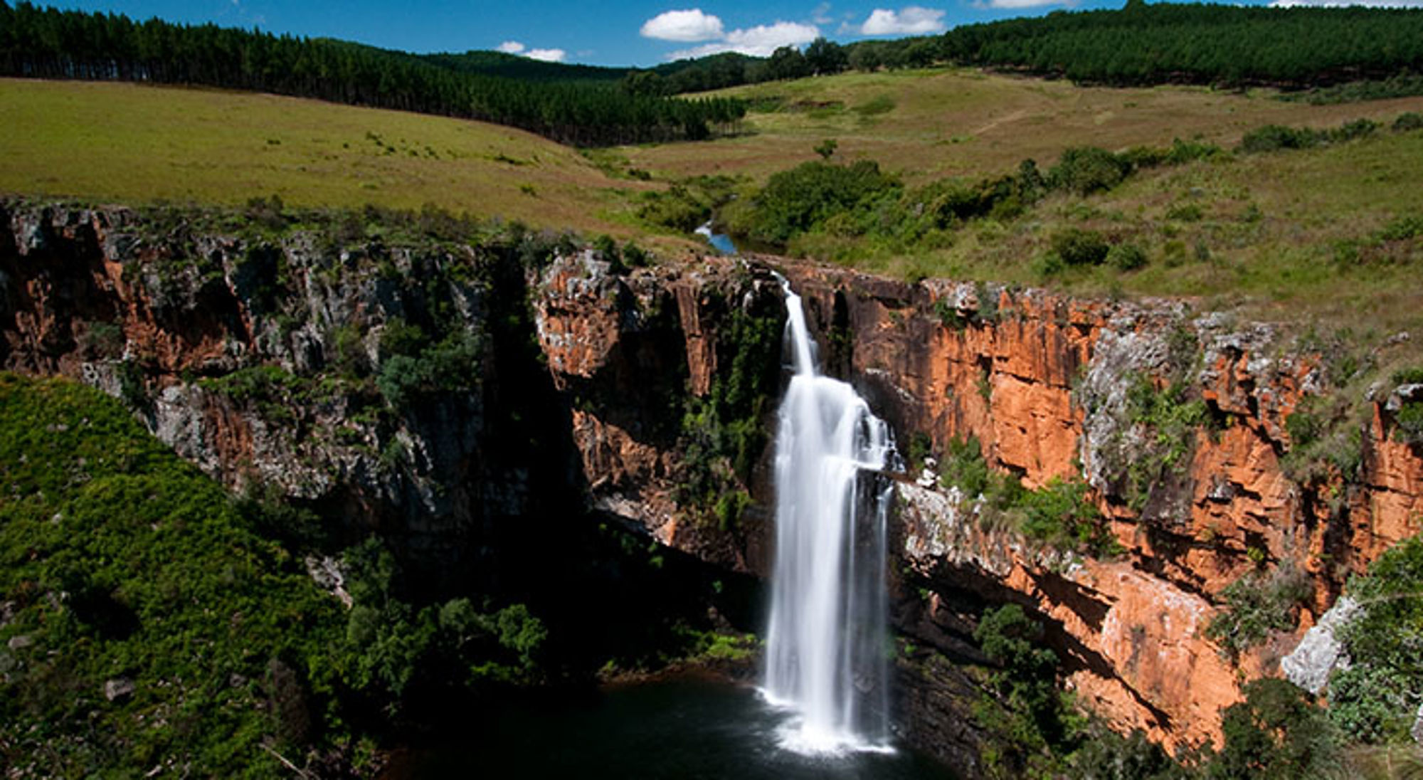 Waterval in een diepe kloof met rode rotswanden en groen landschap in Zuid-Afrika.