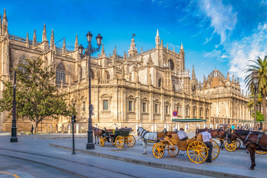 Kathedraal van Sevilla in Andalusië met paardenkoetsen op het plein onder een heldere blauwe lucht.