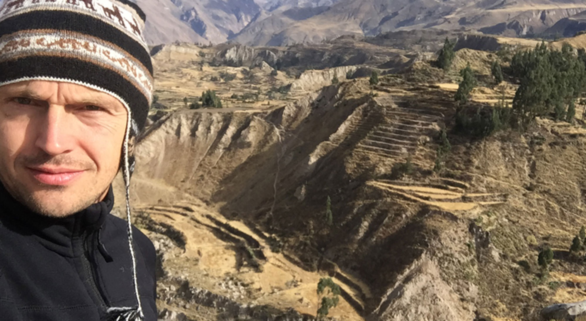 Bastiaan bij de Colca Canyon Man met muts poseert voor berglandschap met terrassen en valleien.