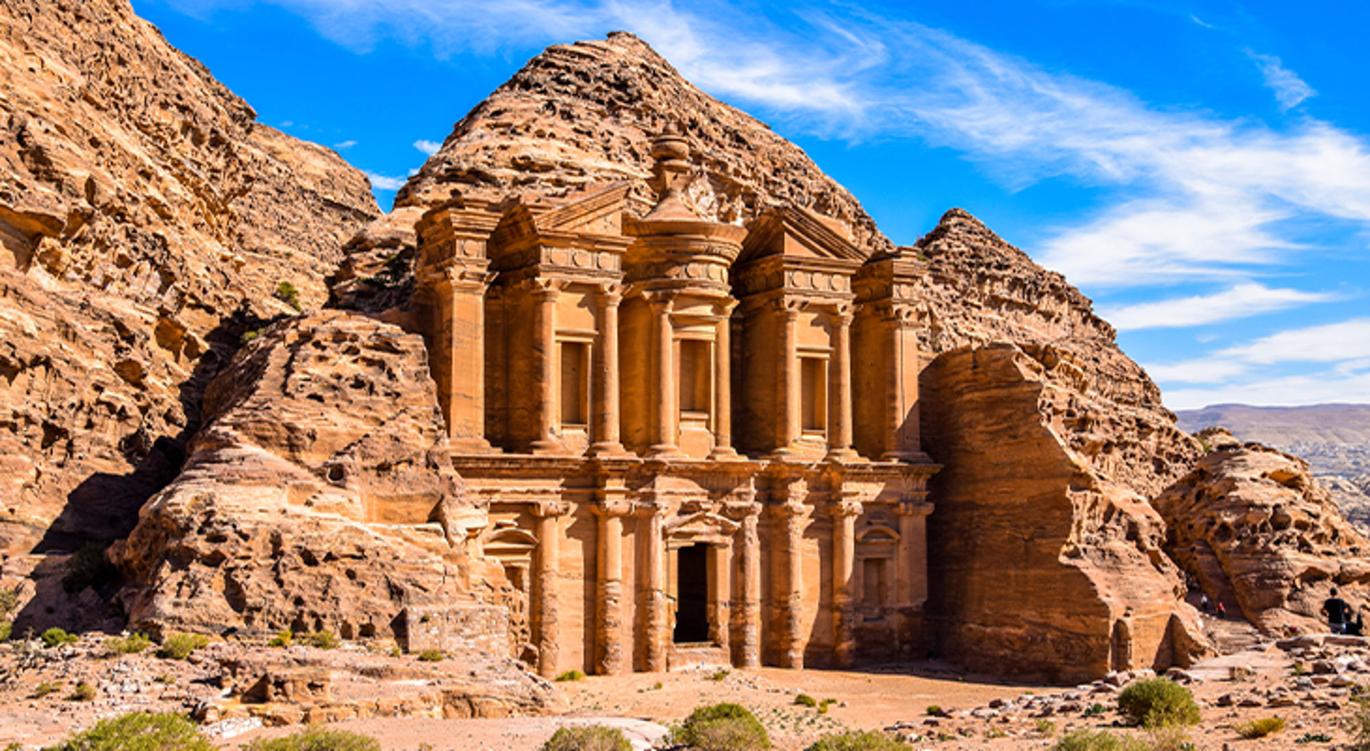 Petra in Jordanië - 7 nieuwe wereldwonderen De rotsuitgehouwen gevel van het Klooster (Ad Deir) in Petra, Jordanië, onder een blauwe lucht.