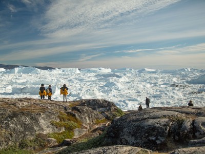 Wandelaars op rotsen met uitzicht op een uitgestrekt ijslandschap in Canada en Groenland tijdens de 18-daagse route.